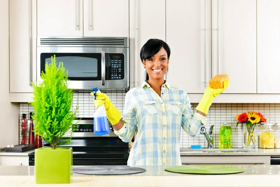 Smiling house cleaner Fort Myers holding spray bottle and sponge in clean kitchen
