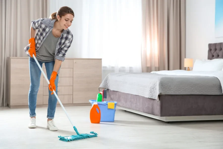 A girl mopping bedroom floor with cleaning supplies bucket nearby