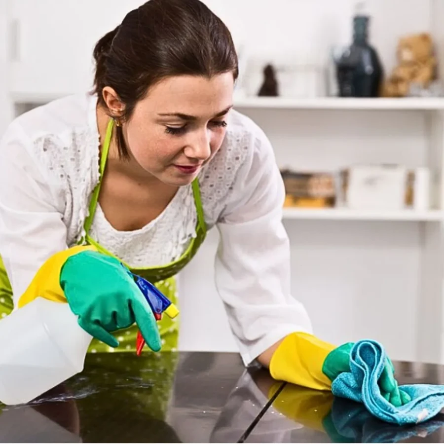 Maid spraying and wiping dark countertop surface with microfiber cloth and cleaning solution